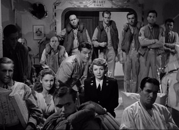 Movie still from “So Proudly We Hail” (1990), directed by Lionel Chetwynd – A group of men and a woman standing next to each other in a room; Wide shot, High angle