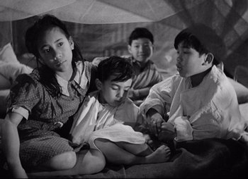 Movie still from “So Proudly We Hail” (1990), directed by Lionel Chetwynd – A group of children sitting on the ground; Medium shot, High angle