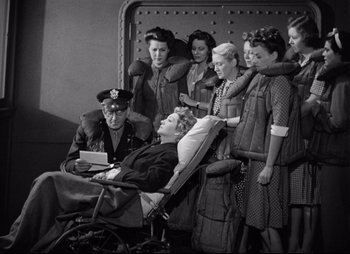 Movie still from “So Proudly We Hail” (1990), directed by Lionel Chetwynd – An old photo of a group of women and a man in a wheel chair; Wide shot, High angle