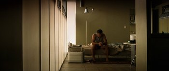 Movie still from “Solaris” (2002), directed by Steven Soderbergh – A man sitting on top of a bed next to a lamp; Wide shot, Low angle