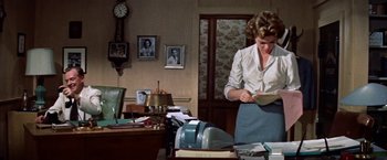 Movie still from “Some Came Running” (1958), directed by Vincente Minnelli – A woman standing in front of a desk holding papers; Medium shot, Low angle