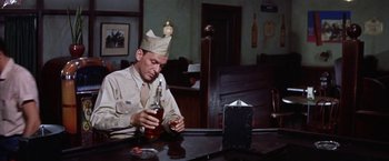 Movie still from “Some Came Running” (1958), directed by Vincente Minnelli – A man sitting at a table with a bottle of alcohol; Medium shot, Low angle