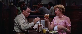 Movie still from “Some Came Running” (1958), directed by Vincente Minnelli – A man and a woman sitting at a table with a hot dog and condiments in front of them; Medium shot, Over the shoulder angle
