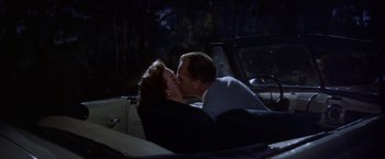 Movie still from “Some Came Running” (1958), directed by Vincente Minnelli – A man and a woman kissing in the back of a car at night; Medium shot, High angle