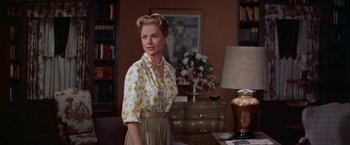 Movie still from “Some Came Running” (1958), directed by Vincente Minnelli – A woman standing in front of a table in a living room; Medium shot, Low angle