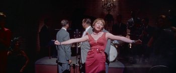 Movie still from “Some Came Running” (1958), directed by Vincente Minnelli – A woman in a red dress singing in front of a crowd; Medium shot, Low angle