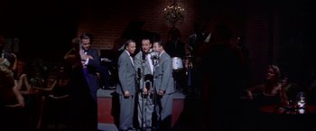 Movie still from “Some Came Running” (1958), directed by Vincente Minnelli – A group of men standing next to each other on a stage with microphones; Wide shot, High angle