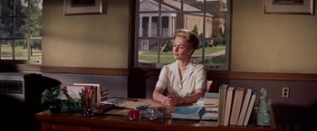 Movie still from “Some Came Running” (1958), directed by Vincente Minnelli – A woman sitting at a desk in front of a window; Medium shot, Low angle