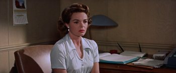 Movie still from “Some Came Running” (1958), directed by Vincente Minnelli – A woman sitting at a desk wearing a white shirt; Close Up shot, Low angle