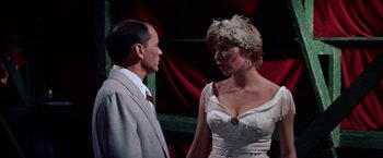 Movie still from “Some Came Running” (1958), directed by Vincente Minnelli – A man and a woman standing next to each other in front of a red curtain; Medium shot, Over the shoulder angle