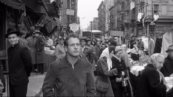 Movie still from “Somebody Up There Likes Me” (1956), directed by Robert Wise – Black and white photograph of a crowd of people walking down a street; Medium shot, Low angle