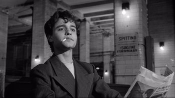 Movie still from “Somebody Up There Likes Me” (1956), directed by Robert Wise – A young man smoking a cigarette while sitting in a chair; Close Up shot, Low angle