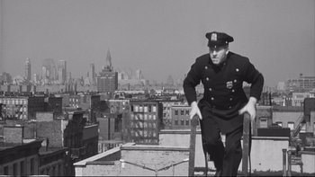 Movie still from “Somebody Up There Likes Me” (1956), directed by Robert Wise – An old photo of a man in a police uniform on the top of a building; Wide shot, Low angle