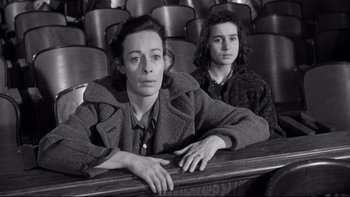 Movie still from “Somebody Up There Likes Me” (1956), directed by Robert Wise – Two people sitting in a theater with one of them leaning on a bench; Medium shot, High angle