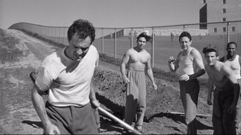 Movie still from “Somebody Up There Likes Me” (1956), directed by Robert Wise – A man holding a baseball bat while standing next to two other men; Medium shot, Low angle