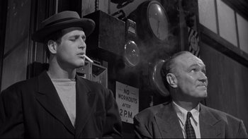 Movie still from “Somebody Up There Likes Me” (1956), directed by Robert Wise – A man smoking a cigarette next to another man in a suit; Medium shot, Low angle