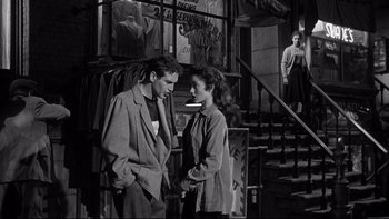 Movie still from “Somebody Up There Likes Me” (1956), directed by Robert Wise – A man and a woman standing next to each other in front of a building; Medium shot, Over the shoulder angle