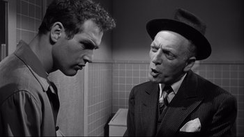 Movie still from “Somebody Up There Likes Me” (1956), directed by Robert Wise – A man in a suit and a man in a hat in a bathroom; Medium shot, Over the shoulder angle