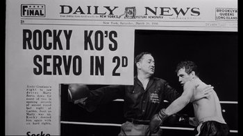 Movie still from “Somebody Up There Likes Me” (1956), directed by Robert Wise – An old photo of two men boxing in front of a newspaper article; Medium shot, Low angle