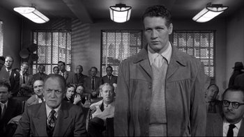 Movie still from “Somebody Up There Likes Me” (1956), directed by Robert Wise – Black and white photograph of a man standing in front of a group of people; Medium shot, Low angle
