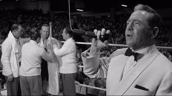 Movie still from “Somebody Up There Likes Me” (1956), directed by Robert Wise – A man in a boxing ring holding a microphone; Medium shot, Low angle