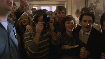 Movie still from “Someone to Watch Over Me” (1987), directed by Ridley Scott – A man taking a picture of a group of people in a room; Medium shot, High angle