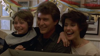 Movie still from “Someone to Watch Over Me” (1987), directed by Ridley Scott – A man and a woman and a child smiling for the camera; Medium shot, Low angle