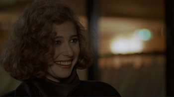 Movie still from “Someone to Watch Over Me” (1987), directed by Ridley Scott – A woman with curly brown hair smiling for the camera; Close Up shot, Over the shoulder angle