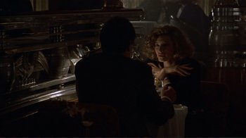 Movie still from “Someone to Watch Over Me” (1987), directed by Ridley Scott – Two people sitting at a table in front of an oven; Medium shot, Over the shoulder angle