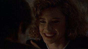 Movie still from “Someone to Watch Over Me” (1987), directed by Ridley Scott – A person with curly hair smiling; Close Up shot, Over the shoulder angle