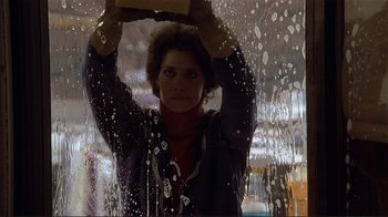 Movie still from “Someone to Watch Over Me” (1987), directed by Ridley Scott – A woman in a black shirt is holding a window cleaner; Medium shot, Low angle
