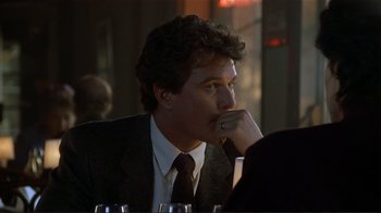Movie still from “Someone to Watch Over Me” (1987), directed by Ridley Scott – A man sitting at a table with his hand under his chin; Close Up shot, Over the shoulder angle
