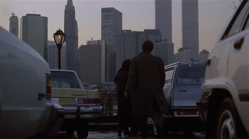 Movie still from “Someone to Watch Over Me” (1987), directed by Ridley Scott – A man and a woman standing in front of parked cars; Wide shot, Over the shoulder angle