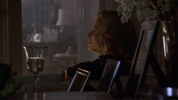 Movie still from “Someone to Watch Over Me” (1987), directed by Ridley Scott – A woman sitting at a table in a dark room; Medium shot, Over the shoulder angle