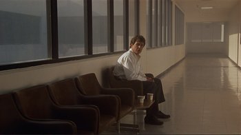 Movie still from “Someone to Watch Over Me” (1987), directed by Ridley Scott – A man sitting in a waiting room next to a window; Wide shot, Over the shoulder angle
