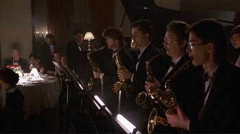 Movie still from “Someone to Watch Over Me” (1987), directed by Ridley Scott – A group of men in black suits playing musical instruments; Wide shot, Low angle