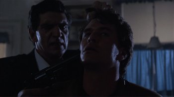 Movie still from “Someone to Watch Over Me” (1987), directed by Ridley Scott – A man is getting his hair cut by a man with a gun; Close Up shot, Low angle
