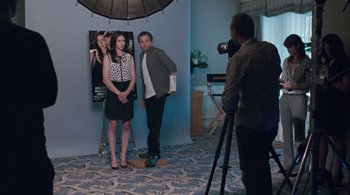 Movie still from “Somewhere” (2010), directed by Sofia Coppola – A man and a woman posing in front of a movie poster; Wide shot, Over the shoulder angle