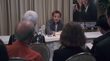 Movie still from “Somewhere” (2010), directed by Sofia Coppola – A man sitting in front of a group of people at a table; Medium shot, Over the shoulder angle