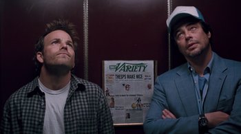 Movie still from “Somewhere” (2010), directed by Sofia Coppola – Two men standing next to each other in front of a variety advertisement; Medium shot, Low angle
