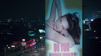 Movie still from “Somewhere” (2010), directed by Sofia Coppola – A billboard of a woman laying on the ground in front of a city street at night; Medium shot, High angle