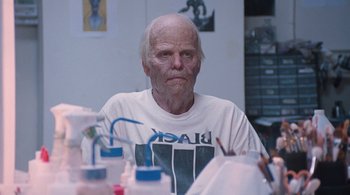 Movie still from “Somewhere” (2010), directed by Sofia Coppola – An old man with a shaved head sitting in front of a table; Close Up shot, Low angle