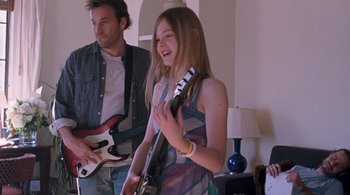 Movie still from “Somewhere” (2010), directed by Sofia Coppola – A woman holding a guitar while standing next to a man; Medium shot, Over the shoulder angle