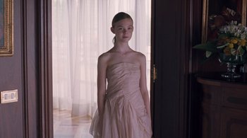 Movie still from “Somewhere” (2010), directed by Sofia Coppola – A young girl in a dress standing in front of a window; Medium shot, Over the shoulder angle
