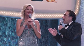 Movie still from “Somewhere” (2010), directed by Sofia Coppola – A woman in a silver dress holding a microphone and a man in a black suit; Medium shot, Over the shoulder angle
