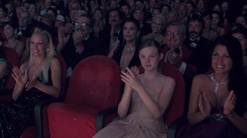 Movie still from “Somewhere” (2010), directed by Sofia Coppola – A girl clapping at a movie theater with many people watching it; Medium shot, Over the shoulder angle