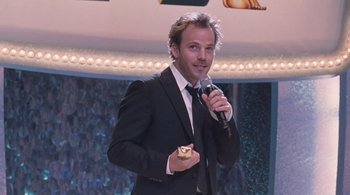 Movie still from “Somewhere” (2010), directed by Sofia Coppola – A man in a black suit holding a microphone; Medium shot, Over the shoulder angle