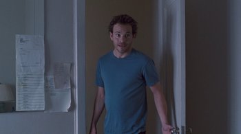 Movie still from “Somewhere” (2010), directed by Sofia Coppola – A man standing in front of a door wearing a blue t - shirt; Medium shot, Over the shoulder angle