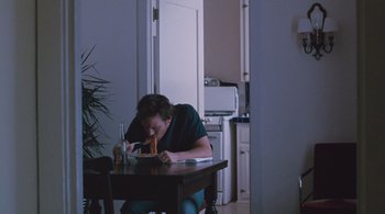 Movie still from “Somewhere” (2010), directed by Sofia Coppola – A man sitting at a dining room table eating a piece of pizza; Wide shot, High angle