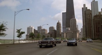 Movie still from “Somewhere in Time” (1980), directed by Jeannot Szwarc – A group of cars driving down a street with tall skyscrapers in the background; Extreme Wide shot, Low angle